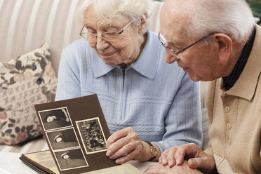 Senior couple watching old photograph album at home - BIF000274