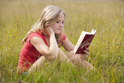 Austria, Salzkammergut, Mondsee, young woman reading book in a meadow - WWF003173