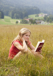 Austria, Salzkammergut, Mondsee, young woman reading book in a meadow - WWF003174