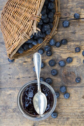 Weidenkorb mit Blaubeeren (Vaccinium myrtillus) und Glas mit Blaubeermarmelade auf Holztisch - LVF000432