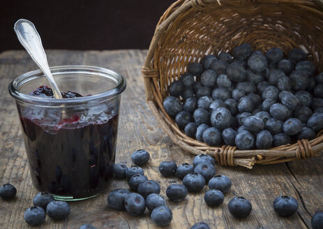 Weidenkorb mit Blaubeeren (Vaccinium myrtillus) und Glas mit Blaubeermarmelade auf Holztisch - LVF000430