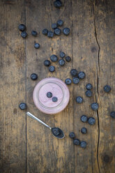 Blueberries (Vaccinium myrtillus), spoon and glass of blueberry yoghurt on wooden table - LVF000427