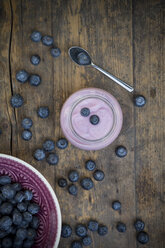 Blueberries (Vaccinium myrtillus), spoon and glass of blueberry yoghurt on wooden table - LVF000426