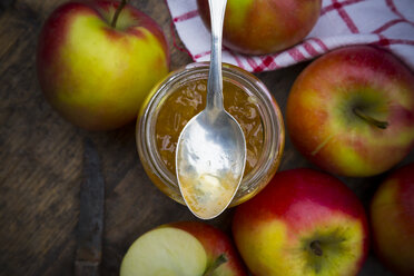 Glass of selfmade apple jam, spoon and apples on wooden table - LVF000417