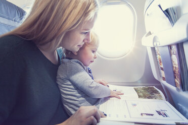 Mutter mit Sohn im Flugzeug beim Lesen einer Zeitschrift - MF000727