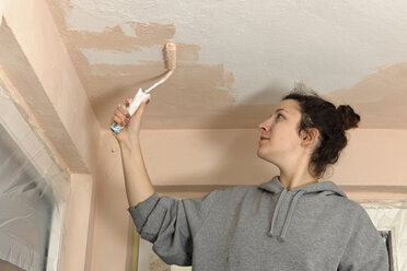 Young woman painting ceiling of an apartment - LAF000402