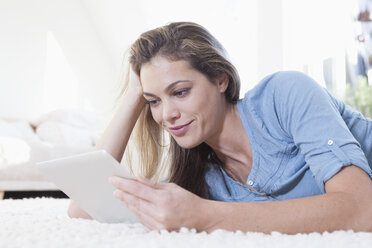 Portrait of woman lying on a carpet using tablet computer - RBF001590