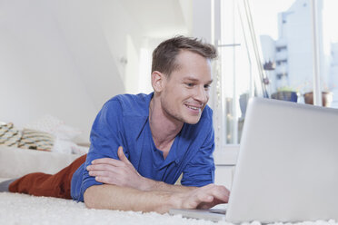 Man at home lying on carpet and using laptop - RBF001533