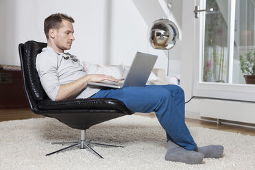 Mann zu Hause im Sessel mit Laptop entspannt - RBF001540