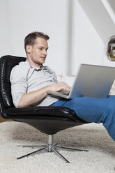 Mann zu Hause im Sessel mit Laptop entspannt - RBF001541