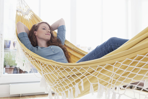 Frau entspannt in einer Hängematte in ihrer Wohnung, lizenzfreies Stockfoto