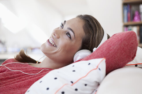 Portrait of woman with headphones lying on a couch in her apartment - RBF001562