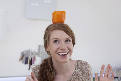 Junge Frau balanciert orangefarbene Paprika auf ihrem Kopf, lizenzfreies Stockfoto