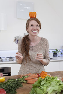 Junge Frau balanciert orangefarbene Paprika auf ihrem Kopf - RBF001522