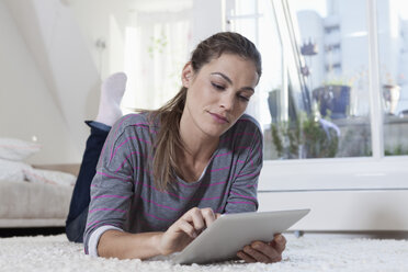 Frau zu Hause auf Teppich liegend und mit Tablet-Computer - RBF001504