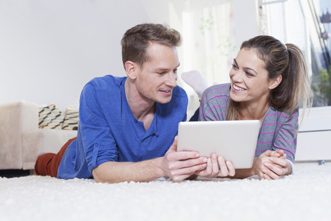 Paar zu Hause auf Teppich liegend und mit Tablet-Computer, lizenzfreies Stockfoto