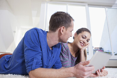 Couple at home lying on carpet and using tablet computer - RBF001502