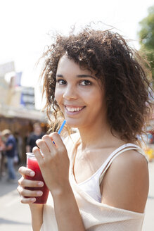 Germany, Herne, Young woman at fairground drinking juice, portrait - BGF000080