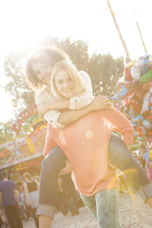 Germany, Herne, Two young women at the fairground carrying each other piggyback - BGF000062