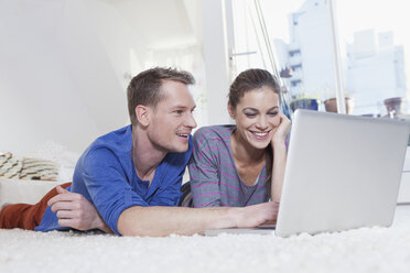 Couple lying on carpet at home using laptop - RBF001499