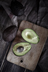 Sliced and whole avocados on chopping board and wooden table - SBDF000461