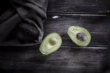 Sliced and whole avocados on chopping board and wooden table - SBDF000463