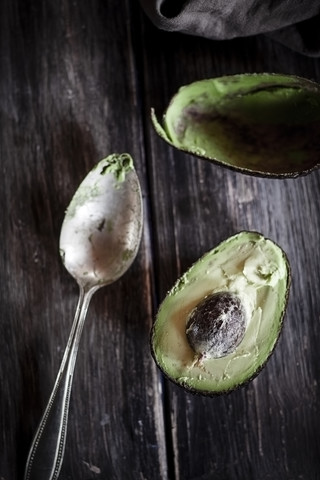 Kitchen towel, spoon and sliced and hollowed halfs of an avocado on wooden table stock photo