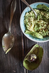 Schale mit zerdrückter Avocado, Löffel und ausgehöhlte Avocadohälfte auf Holztisch - SBDF000466