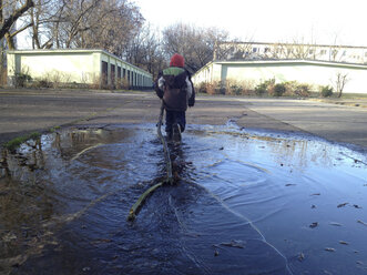 Einfache Kinderspiele: Einen riesigen Stock durch eine Pfütze tragen, Berlin, Deutschland - ZMF000092