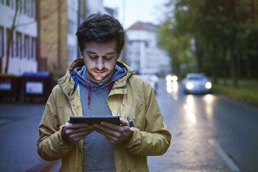 Deutschland, Nordrhein-Westfalen, Köln, junger Mann steht auf der Straße und benutzt ein digitales Tablet - FEXF000065