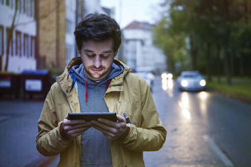 Germany, North Rhine-Westphalia, Cologne, young man standing on a street using digital tablet - FEXF000065