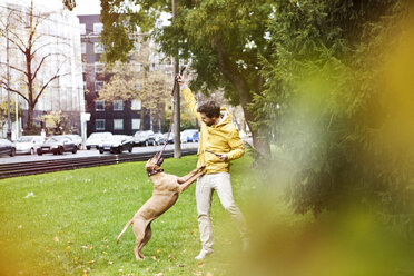 Young man playing with his dog on grass verge - FEXF000070