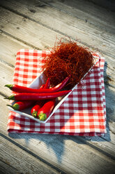 Schale mit roten Chilischoten und Chilifäden auf Küchenhandtuch und Holztisch - MAEF007651