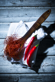 Holzlöffel mit Chilifäden und roten Chilischoten auf Küchenhandtuch und Holztisch - MAEF007660