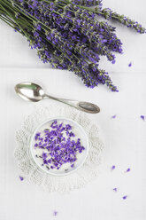 Bowl of natural yoghurt with lavender petals (Lavendula), bunch of lavender and tea spoon on white table cloth - GWF002601