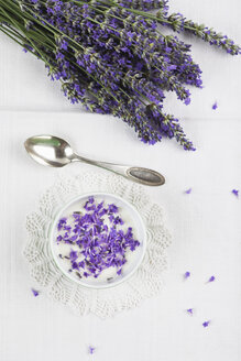 Schale mit Naturjoghurt mit Lavendelblüten (Lavendula), Lavendelsträußchen und Teelöffel auf weißem Tischtuch - GWF002601