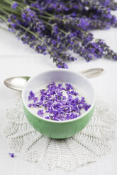 Schale mit Naturjoghurt mit Lavendelblüten (Lavendula), Lavendelsträußchen und Teelöffel auf weißem Tischtuch - GWF002599