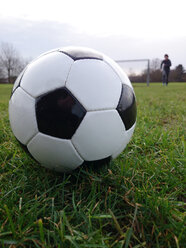 Köln, Nordrhein-Westfalen, Deutschland, Fußball im Gras liegend, junger Mann im Hintergrund - JATF000617