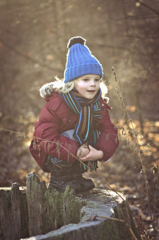 Junge hockt auf Baumstumpf, lizenzfreies Stockfoto