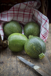 Vier runde Zucchini, ein Küchenhandtuch und ein Taschenmesser auf einem dunklen Holztisch - LVF000481