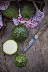 Geschnittene und ganze runde Zucchini, Küchentuch und Taschenmesser auf dunklem Holztisch - LVF000480