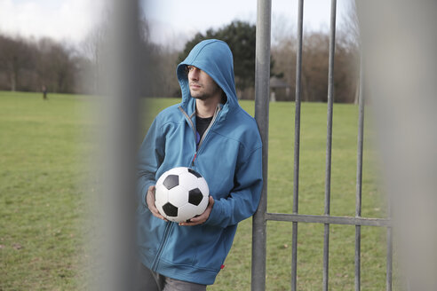 Young man with football leaning at goalpost - JATF000610