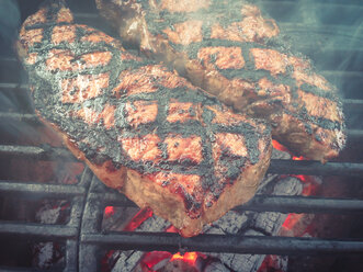 Beef steaks grilling on cast iron barbecue grate over hot charcoal fire - ABAF001192