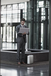 Businessman using laptop in office lobby - CHAF000041