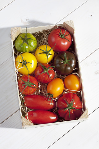 Holzkiste mit verschiedenen Tomaten auf Holztisch, lizenzfreies Stockfoto