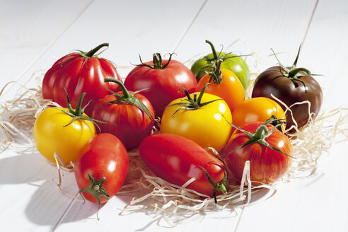 Verschiedene Tomaten auf Holzwolle und Holztisch - CSF020739