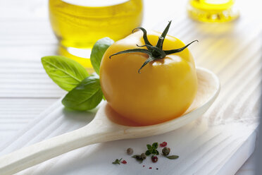 Gelbe Tomate auf Holzlöffel, Olivenöl, Basilikum und Pfefferkörner auf Holztisch - CSF020718