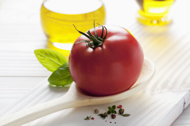 Rote Tomate auf Holzlöffel, Olivenöl, Basilikum und Pfefferkörner auf Holztisch - CSF020681