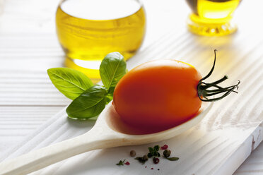 Orangefarbene Tomate auf Holzlöffel, Olivenöl, Basilikum und Pfefferkörner auf Holztisch - CSF020680