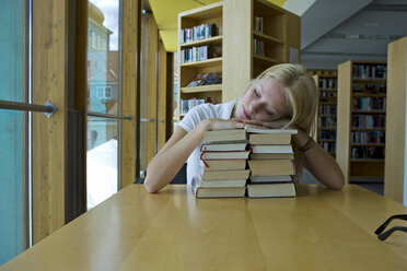 Deutschland, Baden-Württemberg, junge Studentin schlafend auf einem Bücherstapel in einer Bibliothek - CHAF000105